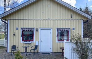 A two-story building with a white door, two windows with red frames, and a small porch area with a table and two chairs. - 1 bedroom cozy home in Färjestaden (Färjestaden)