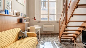 A room with a wooden staircase, a white radiator, a window with a view, a yellow sofa, and a table with chairs. - Sogno Apartment Lucca – Bright Loft in Historic Center, Sleeps 4 (Lucca)