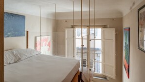 A bedroom with a bed, a window with a view, and a painting on the wall. - Sogno Apartment Lucca – Bright Loft in Historic Center, Sleeps 4 (Lucca)