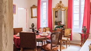 Uma sala de jantar com uma mesa posta para quatro pessoas, rodeada por cadeiras estampadas, um espelho e um vaso sobre uma mesinha lateral.