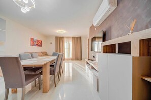 A modern living room with a dining area, a flat-screen TV mounted on the wall, and a built-in air conditioning unit. - Pembroke 2BR Near Sea home |5 min Walk to Beach (Pembroke)