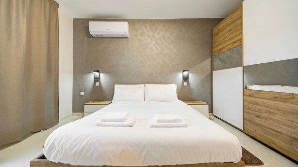 Et moderne hotelværelse med en stor seng, sengeborde, en aircondition og en træsenggavl.
