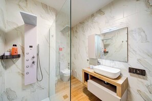 A modern bathroom with a glass-enclosed shower, a white sink, and a marble-tiled wall. - Pembroke 2BR Near Sea home |5 min Walk to Beach (Pembroke)