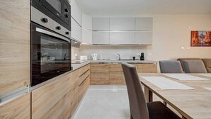 Et moderne køkken med indbyggede hårde hvidevarer, et spiseområde med bord og stole, samt et billede på væggen.