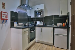 A modern kitchen with a microwave, oven, and refrigerator, white cabinets, and a fire safety sign. - Student Only 136 New Walk (Leicester)