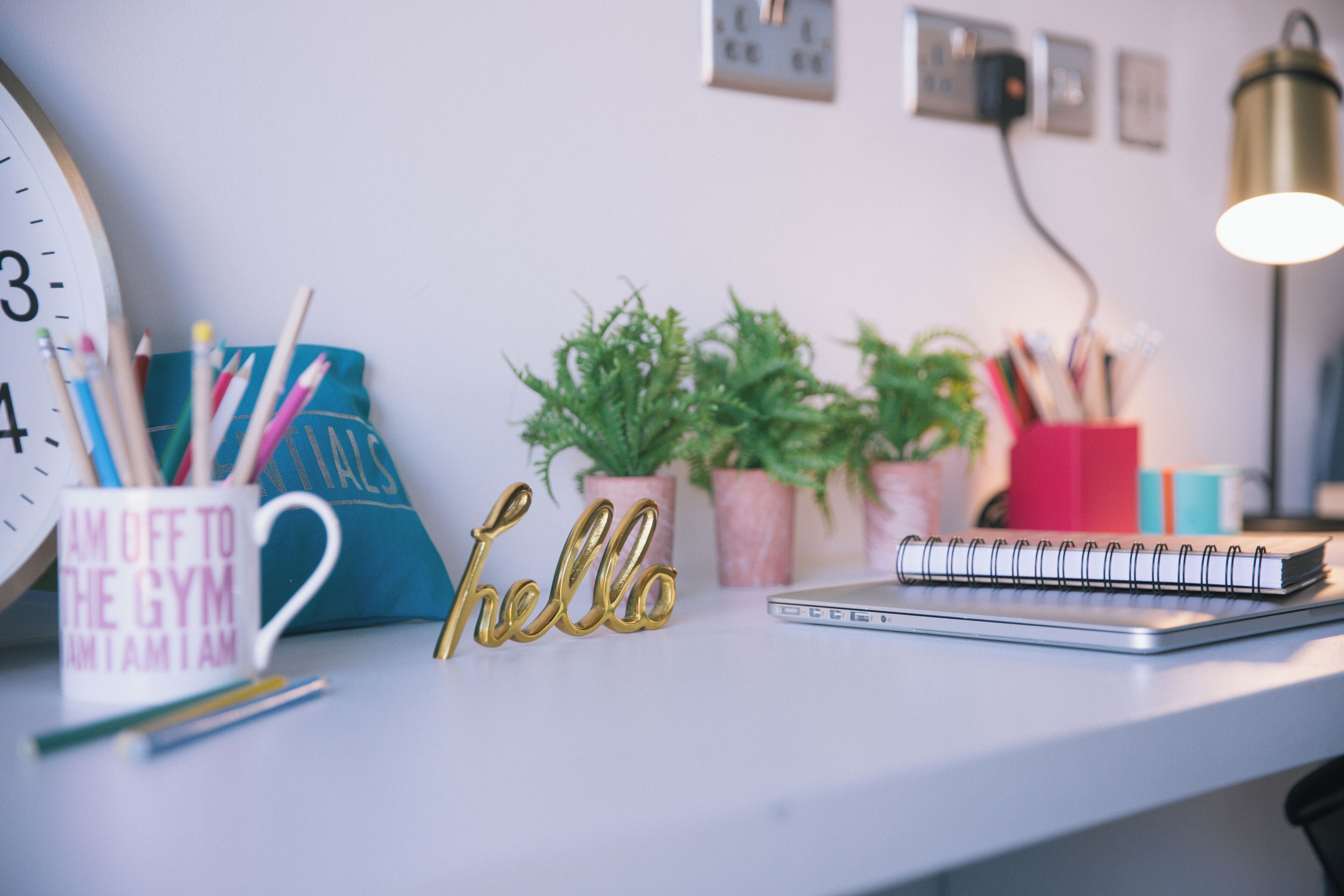 A desk with a clock, a 'hello' sign, a notebook, and potted plants.