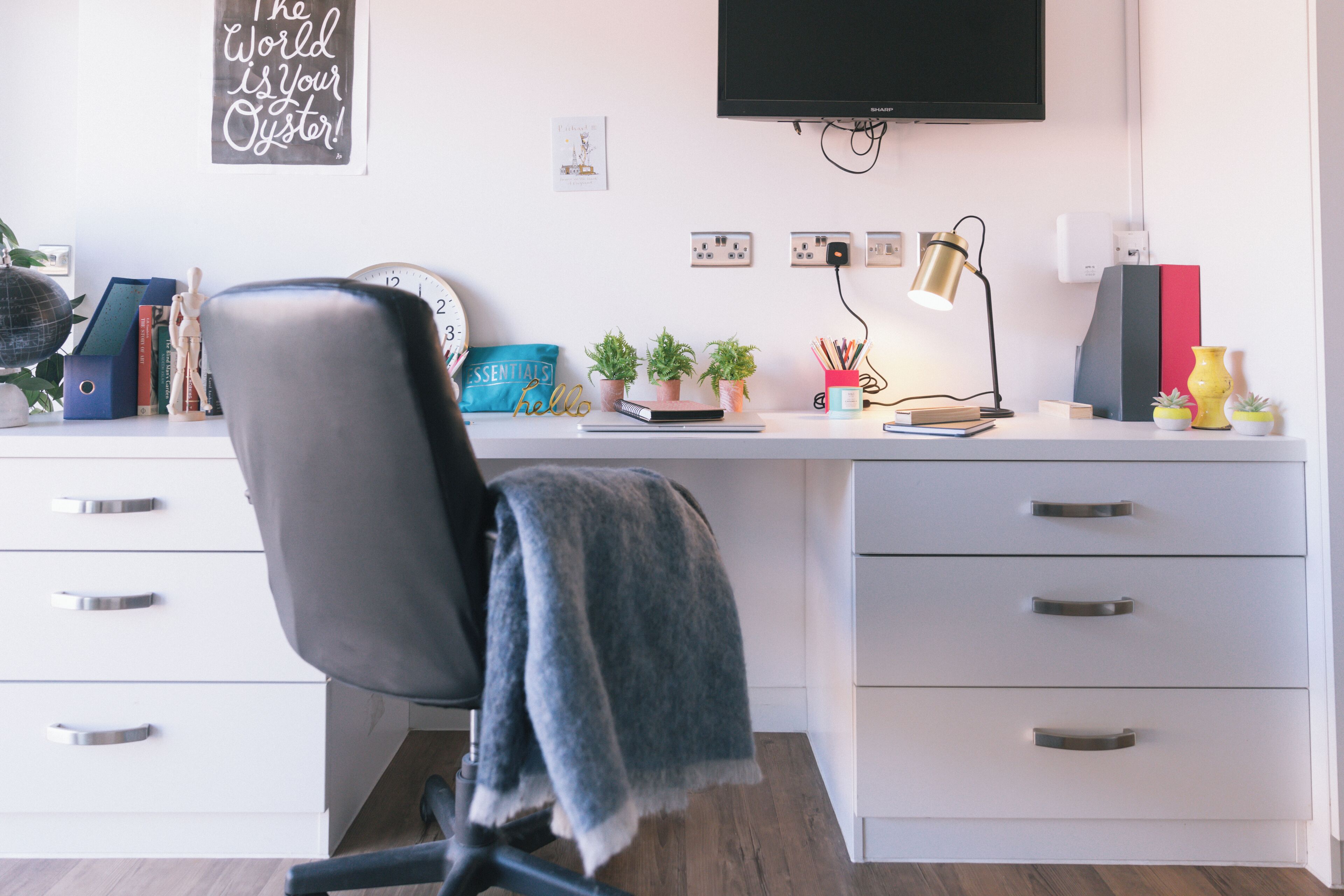 A modern office desk with a chair, a flat-screen TV, a clock, and various decorative items.