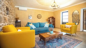 Una sala de estar con pared de piedra, un sofá azul, sillones amarillos, una mesa de centro de madera y una alfombra estampada.