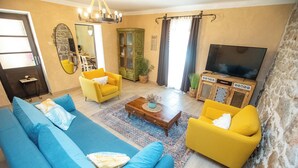 Una sala de estar con sofá, sillones, una mesa de centro, televisor y una pared de piedra.