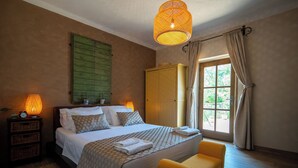 Un dormitorio con cama, lámparas de noche, armario, ventana con cortinas y una banca.