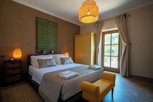 A bedroom with a bed, bedside lamps, a wardrobe, a window with curtains, and a bench.