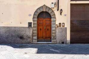 A building with a large wooden double door, a stone archway, and a closed metal shutter to the right. - Paganini Apartment Lucca (Lucca)