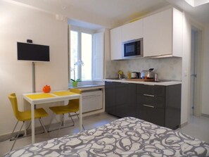 A compact room with a bed, a small dining table with chairs, a kitchenette with a microwave, and a TV mounted on the wall. - Paganini Apartment Lucca (Lucca)