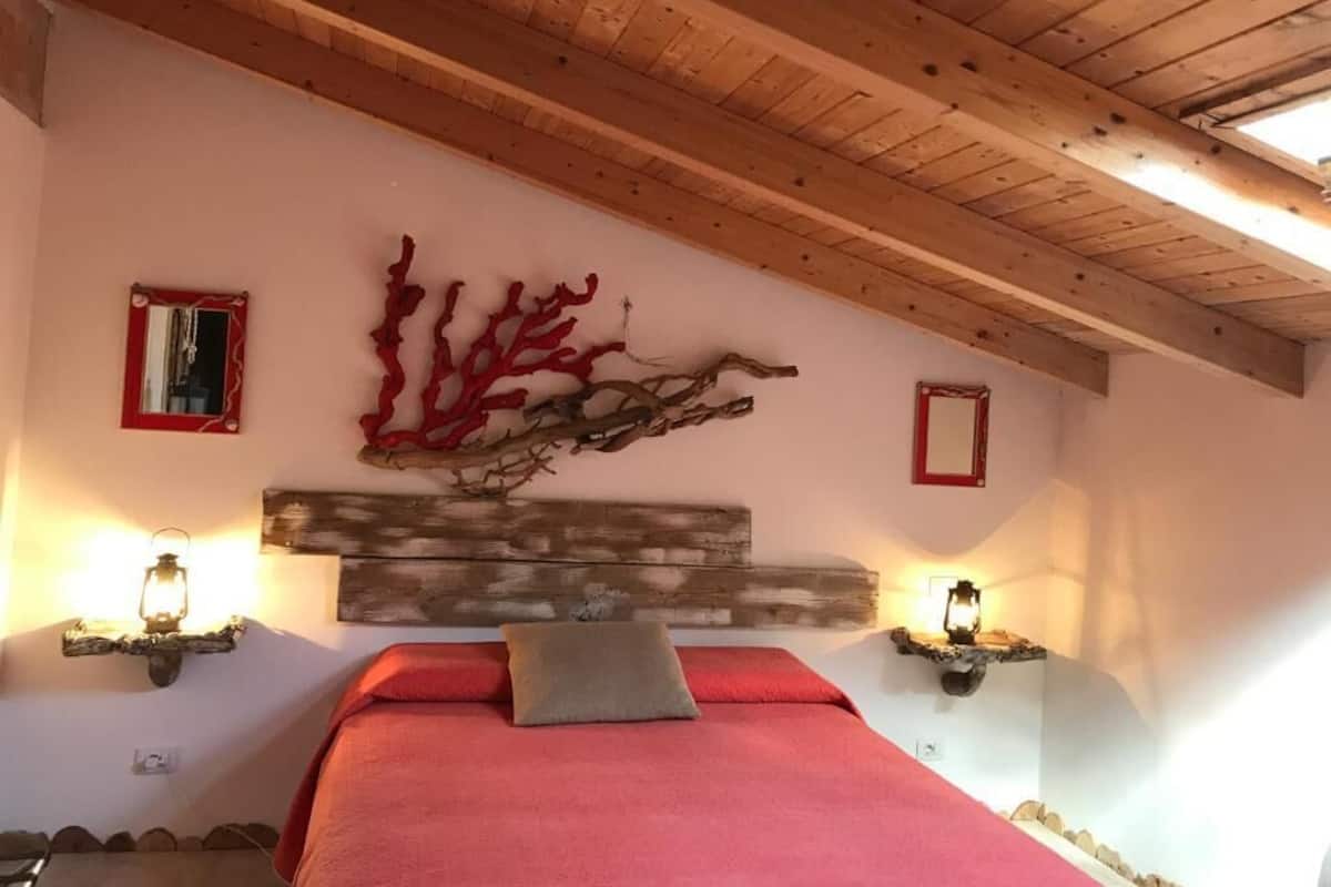 Un dormitorio con techo de madera, cama con ropa de cama roja e iluminación en la pared.