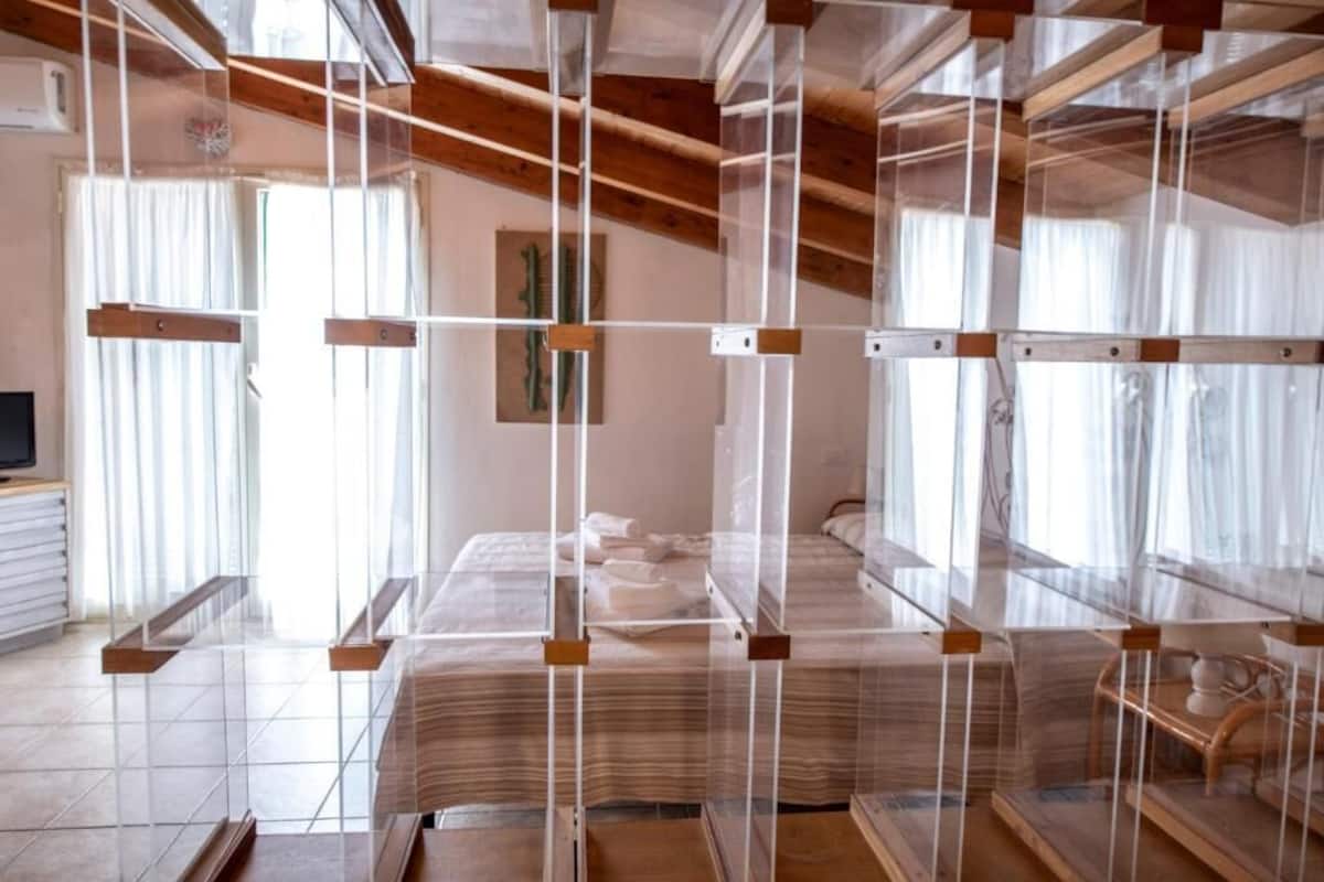 Una habitación con una cama cubierta por un dosel transparente, vigas de madera en el techo y un cuadro en la pared.