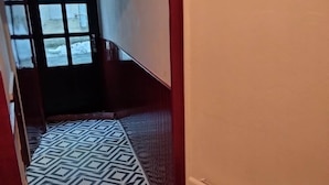 Een gang met vloerbedekking met een patroon, een radiator en een deur die naar buiten leidt.