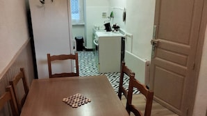 Een eetgedeelte met een houten tafel en stoelen, een keuken op de achtergrond en een vloer met een patroon.