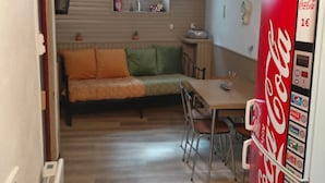 Een compacte woonruimte met een bank, eettafel, stoelen, een koelkast en een raam.
