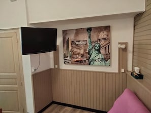 Una habitación con televisión montada en la pared, un cartel con la Estatua de la Libertad y Broadway, y un panel de pared de madera.