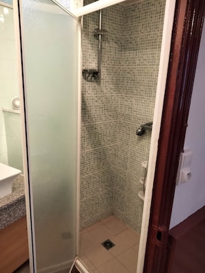 Ducha con puerta de vidrio, paredes de azulejos y ducha.