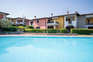 Una piscina con edificios residenciales de varios pisos cercanos, cielos despejados y abundante vegetación bien cuidada.