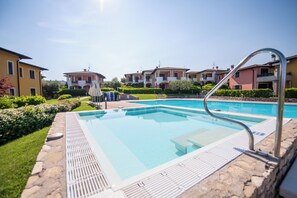 Una piscina con escalera metálica, rodeada de muros de piedra y vegetación, con edificios de varios pisos al fondo.