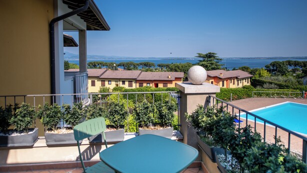 Un balcon donnant sur une piscine, agrémenté de plantes en pot, et offrant une vue sur un ciel bleu dégagé.
