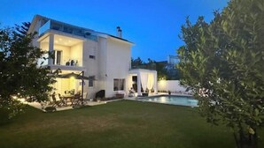 Ein modernes, zweistöckiges Haus mit Swimmingpool, überdachter Terrasse und gepflegtem Rasen.