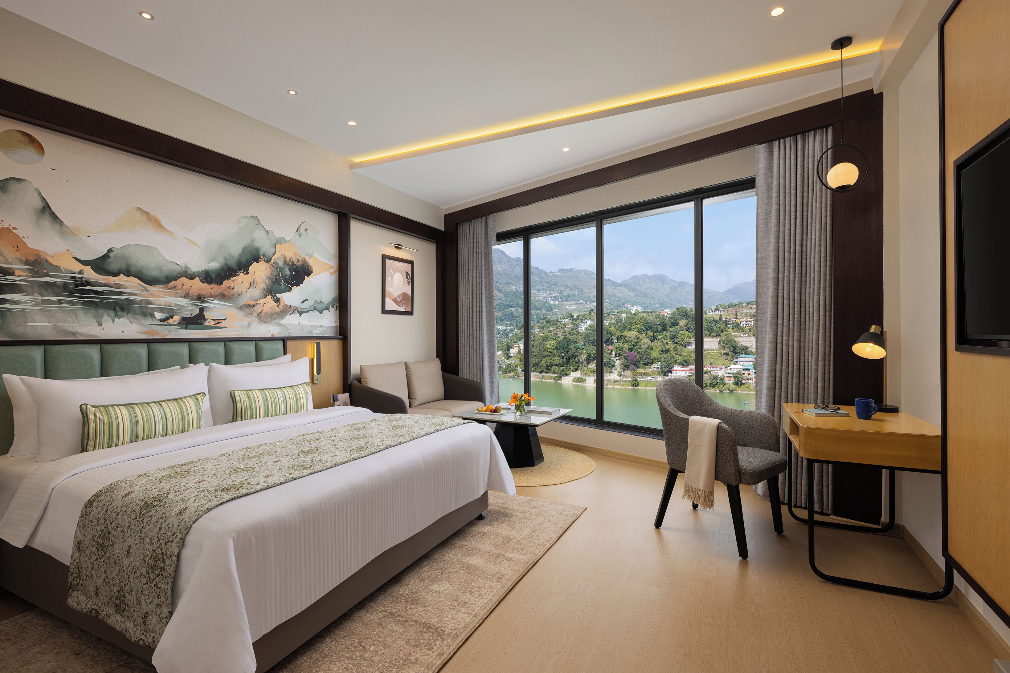 A hotel room with a large bed, a desk, a chair, a view of the mountains, and a painting on the wall.