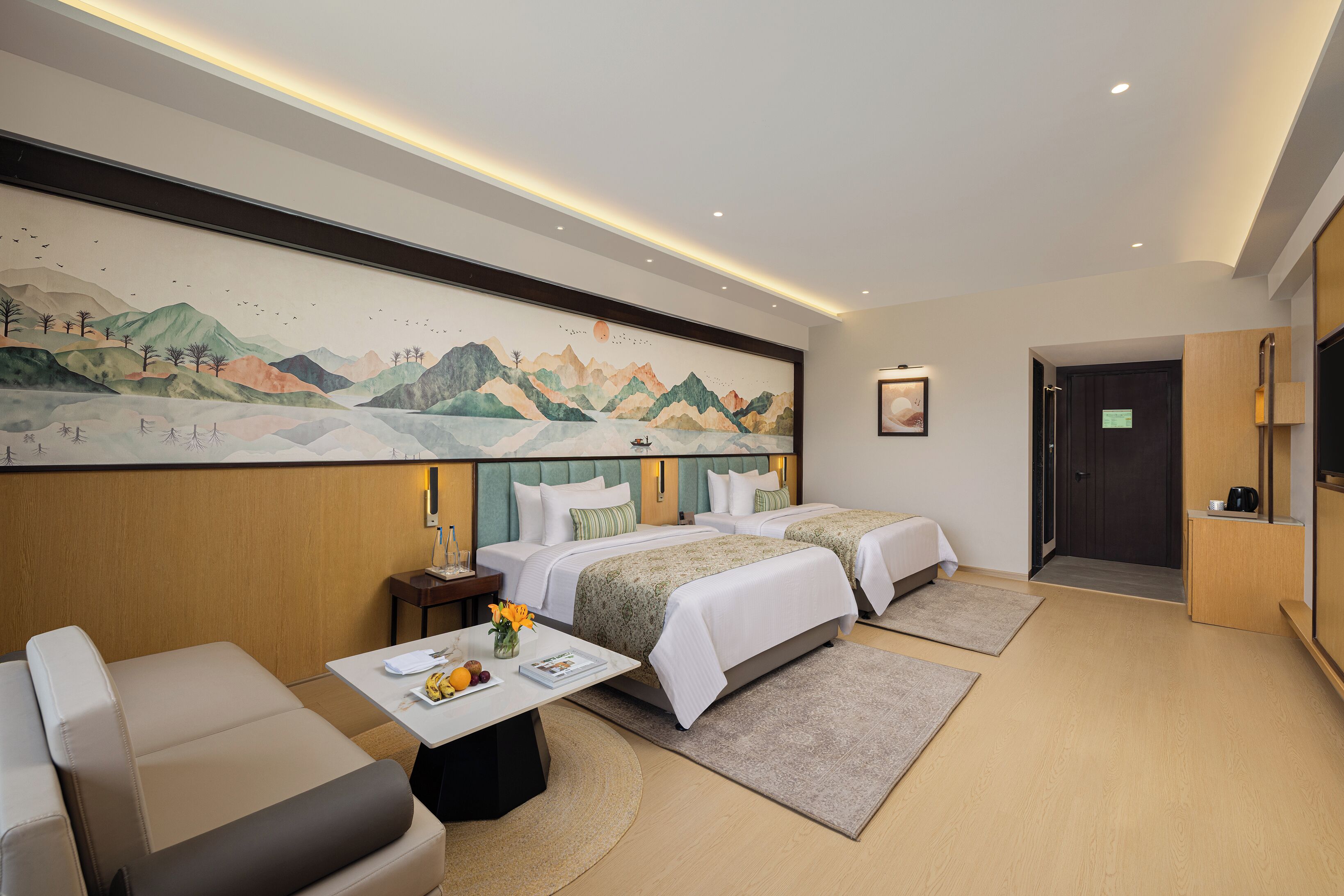 Une chambre d’hôtel avec deux lits, un canapé, une table ornée d’un vase de fleurs et un tableau accroché au mur.