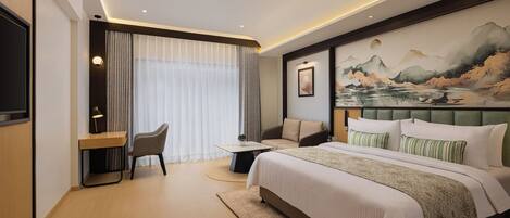 Habitación de hotel con una cama grande, un escritorio, una silla, un sofá y un cuadro en la pared.