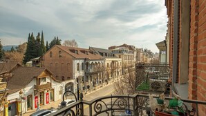 A street view with buildings, a balcony with a railing, and a parked car. - HB apartments Marjani (Tbilisi)