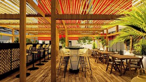 A wooden outdoor seating area with tables and chairs, a bar, and a pergola with red and yellow striped fabric. - Ibis Lagos Lekki (Lekki)