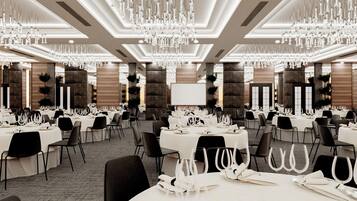 Une salle de banquet avec de nombreuses tables dressées pour le repas, agrémentée de lustres et d’un décor moderne.