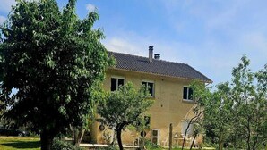 A two-story building with a tiled roof, surrounded by a grassy yard and trees. - Charming house with swimming pool in the heart of Périgord Noir (LE BUGUE 24260) (Le Bugue)