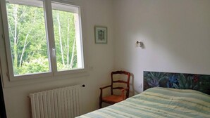 A bedroom with a bed, a chair, a radiator, and a window with a view of trees. - Charming house with swimming pool in the heart of Périgord Noir (LE BUGUE 24260) (Le Bugue)