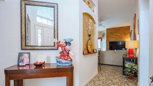 Et værelse med et træbord, et spejl med ramme, en Mickey Mouse-figur, et billede med ramme og et mønstret gulv.