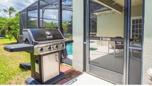 En grill uden for et hus med en glasdør og en pool i baggrunden.