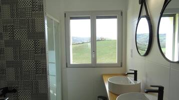 Ein Badezimmer mit zwei Waschbecken, einem Fenster mit Blick auf eine grüne Landschaft und einem duschvorhang mit Muster.