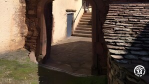 A stone bridge arching over a narrow pathway leading to a building with a tiled roof and a blue door.