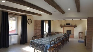 A dining area with a long table, chairs, a clock, and a fireplace.