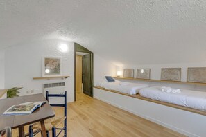 Una stanza con un letto, una scrivania con una sedia, un tavolino e una mensola a parete con delle foto.