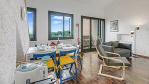 Ein Essbereich mit einem Tisch für vier Personen, einem blau-gelben Stuhl, einem grauen Sofa und einer Stehlampe.