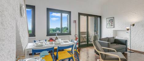 A dining area with a table set for four, a blue and yellow chair, a grey sofa, and a floor lamp.