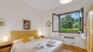 Ein ordentlich bezogenes Bett mit weißen Leinen, einem Holzkopfende und einem Fenster mit Blick auf Grünflächen.