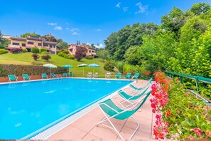 Une piscine entourée de verdure et de bâtiments, avec des chaises longues et des parasols.