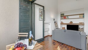 Ein Wohnbereich mit grauem Sofa, einem Tisch mit Früchten und einer Flasche, einer Schiebetür und einem Bücherregal mit Büchern und Dekoration.
