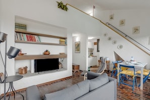 Ein Wohnzimmer mit einer Couch, einem Fernseher, einem Bücherregal und einem Essbereich mit Stühlen und einem Tisch.