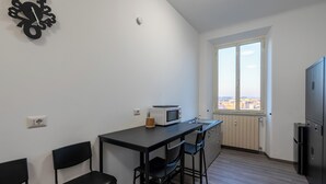 A compact kitchen with a dining area, a window with a city view, and a built-in refrigerator. -  ReRent Rooms - 36 Trionfale Guesthouse (Rome)