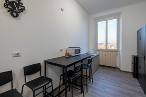 A compact kitchen with a dining area, a window with a city view, and a built-in refrigerator. -  ReRent Rooms - 36 Trionfale Guesthouse (Rome)